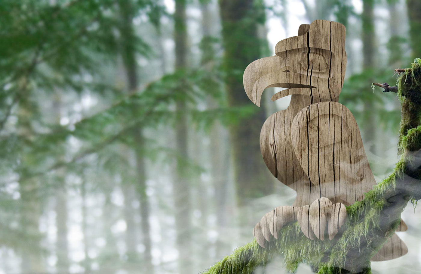 Image of misty woods on the West Coast with a branch covered in lush green moss in the foreground. The branch has a hand-carved wooden eagle statue in the West Coast Style perched upon it.